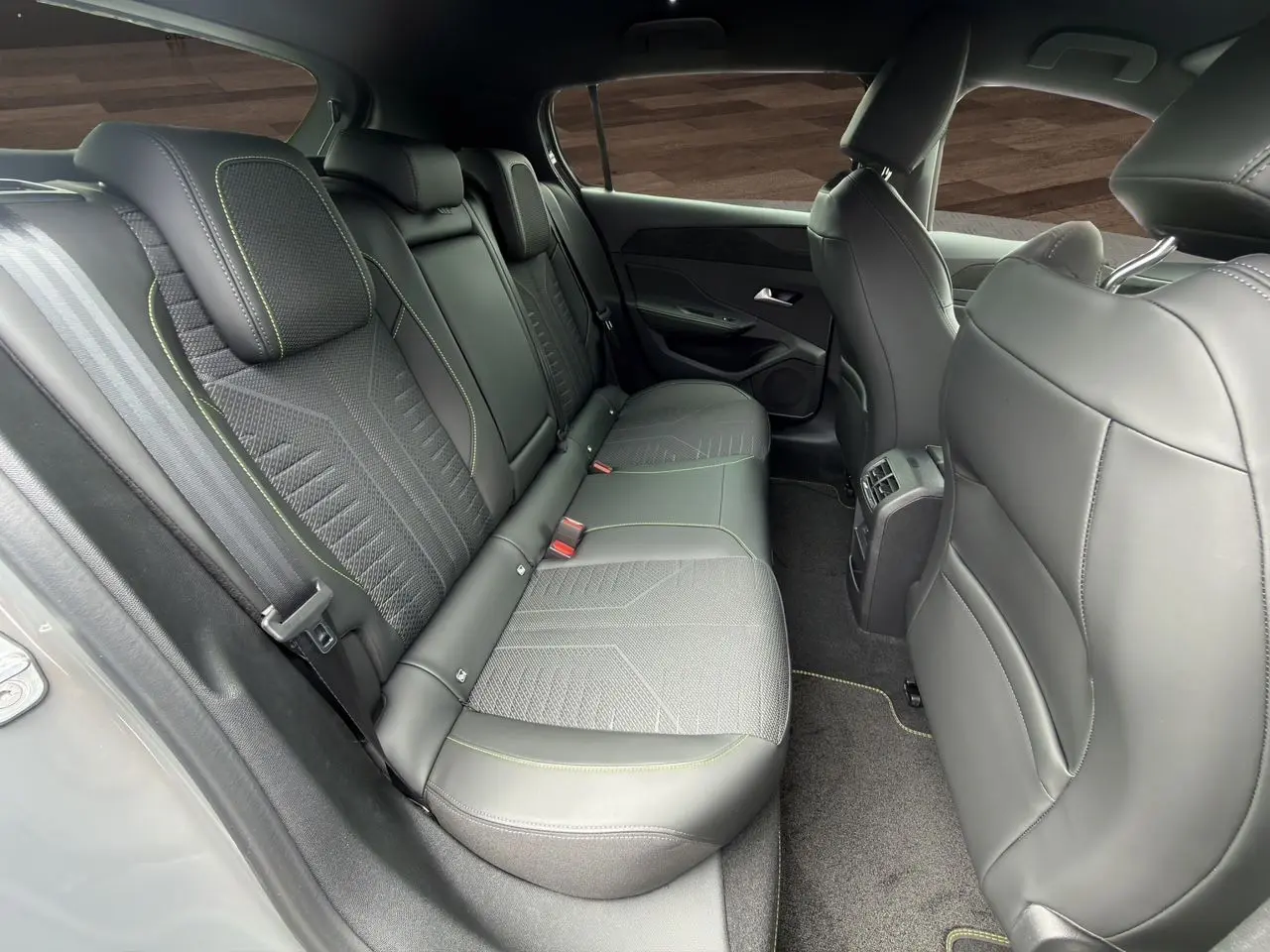 Vue intérieure arrière côté droit de la Peugeot 308 GT 2026, sièges noirs avec surpiqûres vert Adamite et tissu Uzila embossé.