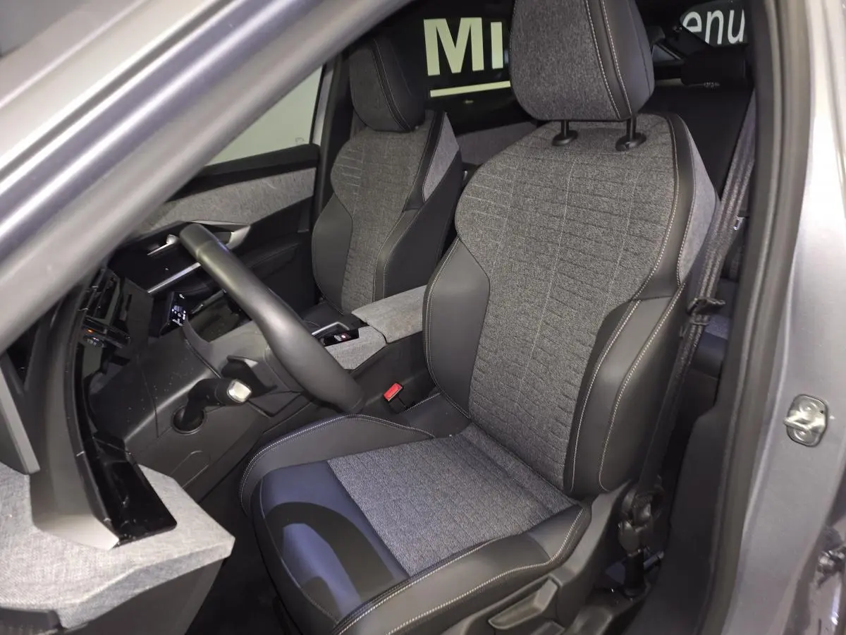 Vue intérieure côté conducteur du Peugeot 3008 gris 2025, sièges tissu gris et cuir noir avec surpiqûres contrastées.