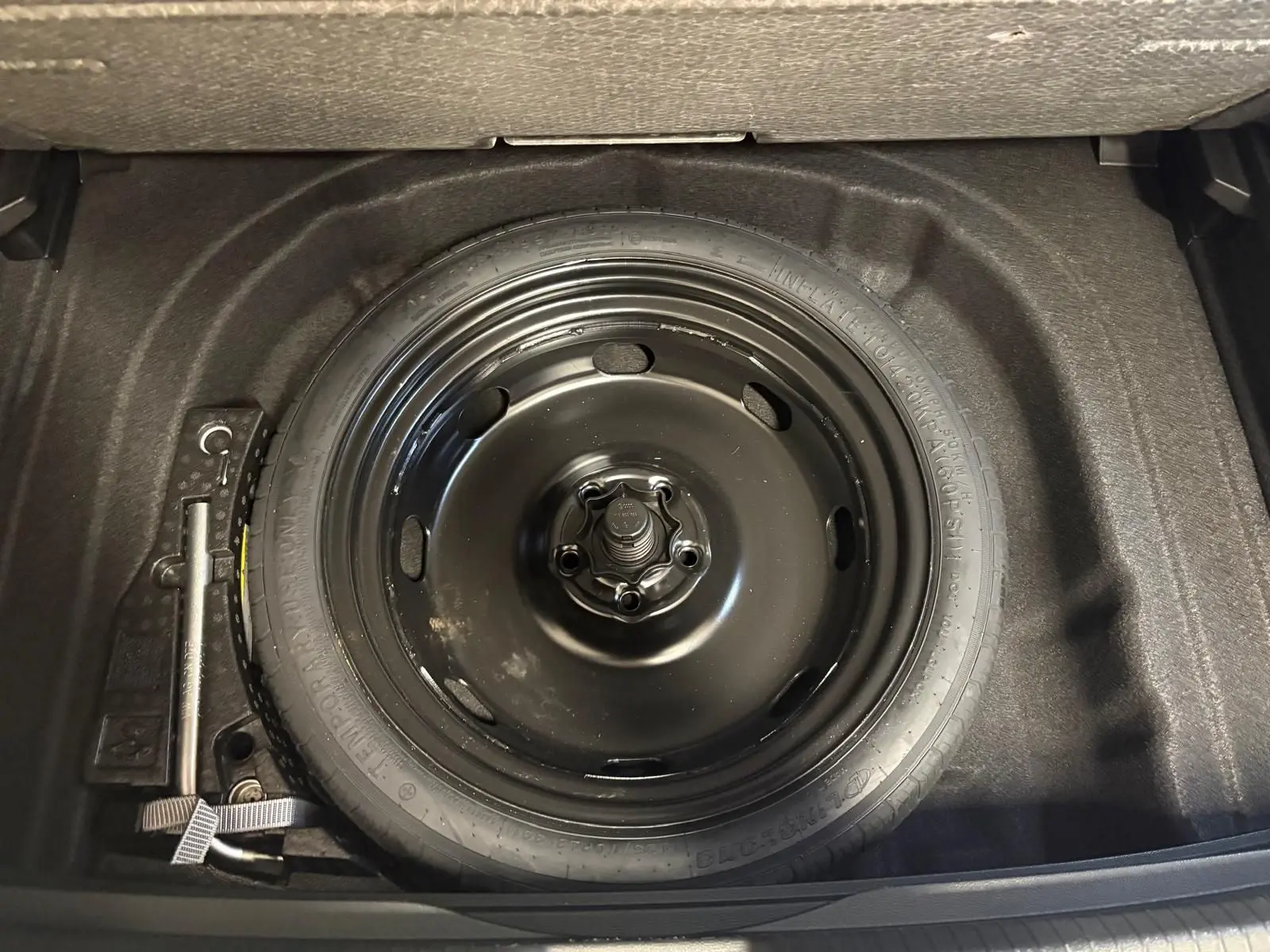 Roue de secours noire en acier dans le coffre d'une Volkswagen Golf 1.5 eTSI 116 DSG7 Bleu Anémone, vue de dessus.