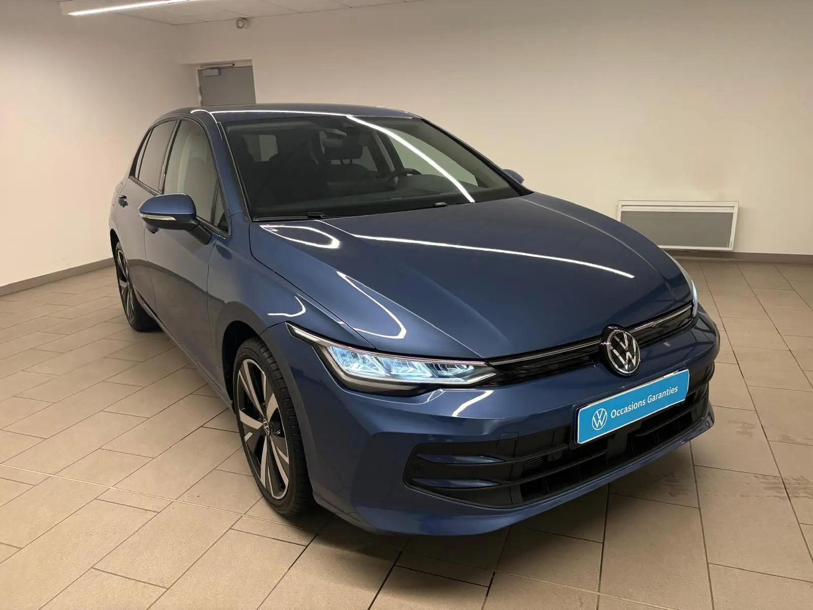 Volkswagen Golf 1.5 eTSI 116 DSG7 Bleu Anémone vue 3/4 avant avec jantes alliage 18'' Catania en intérieur showroom.