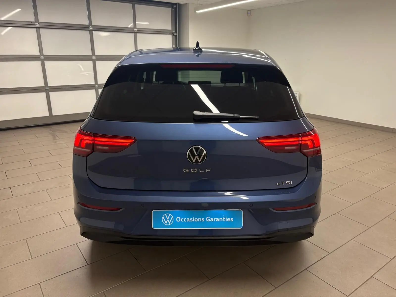 Vue arrière d'une Volkswagen Golf 1.5 eTSI 116 DSG7 en bleu Anémone avec feux arrière allumés dans un garage.