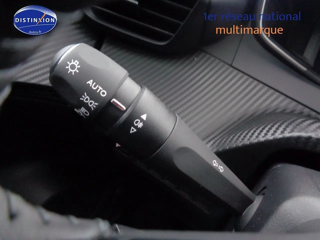 Gros plan sur la commande d'éclairage avec finition carbone dans l'habitacle du Peugeot 2008 rouge Elixir Metal 2023.