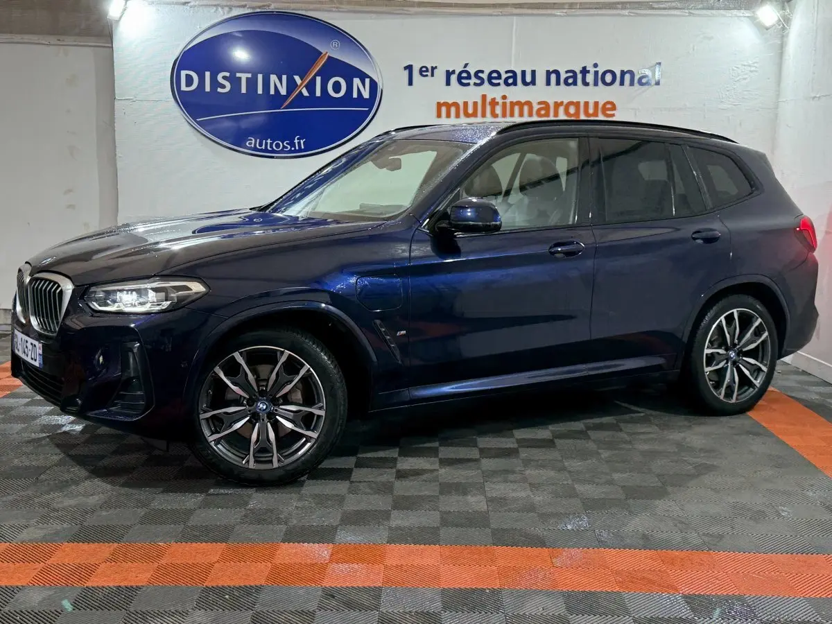 BMW X3 xDrive30e bleu en profil côté gauche dans un showroom avec logo Distinxion en arrière-plan.