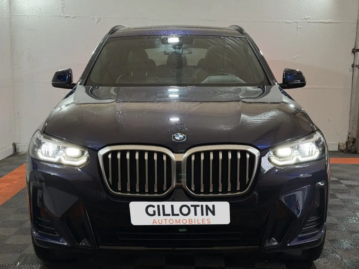 Vue frontale d'un BMW X3 xDrive30e bleu avec phares LED allumés dans un garage.