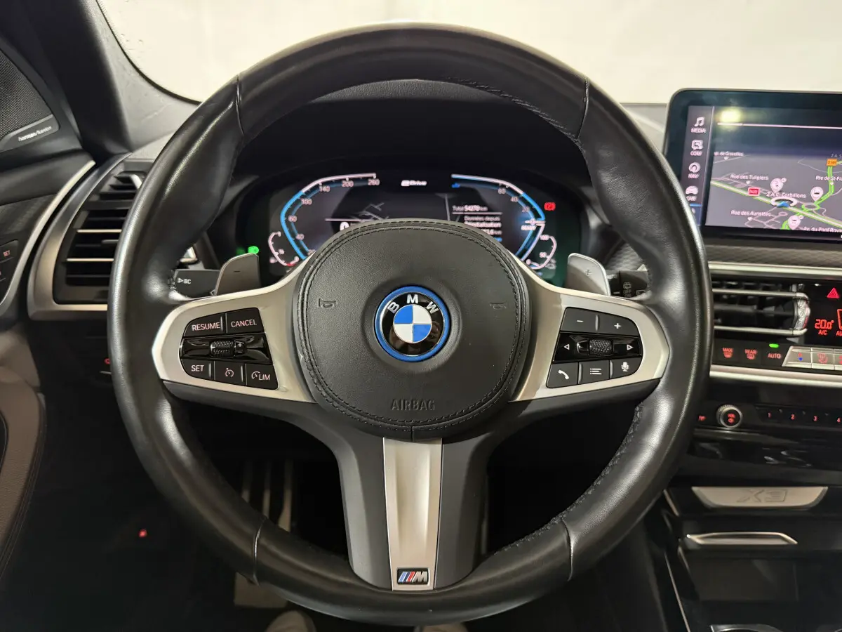 Volant cuir BMW M Sport avec commandes intégrées, tableau de bord numérique et écran tactile de navigation visible.