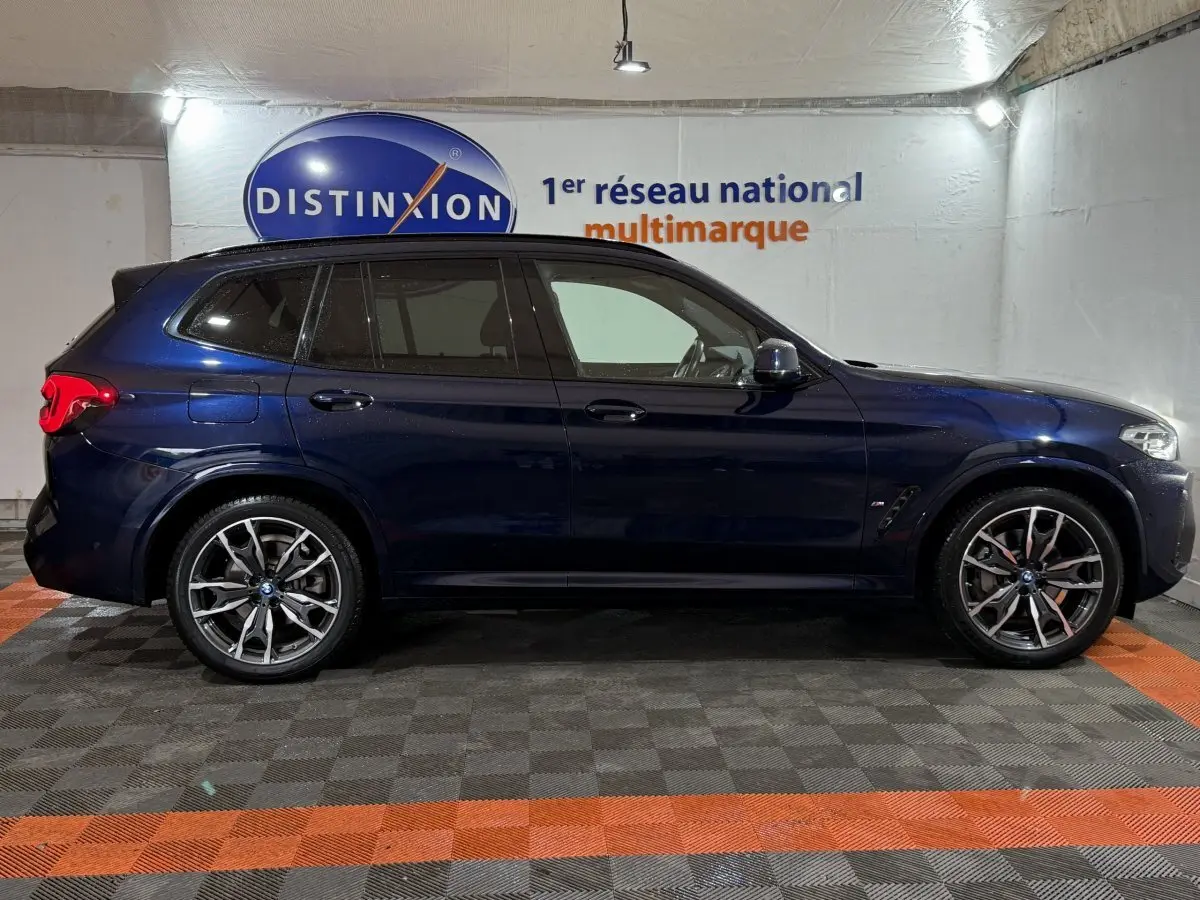 BMW X3 xDrive30e bleu en vue profil côté gauche, avec jantes alliage et vitres teintées dans un showroom.