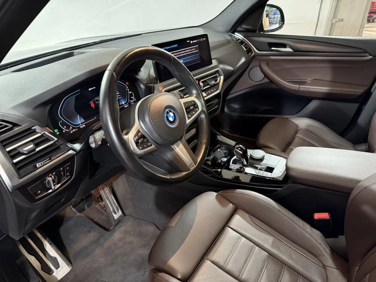 Intérieur BMW X3 xDrive30e 2023 vu côté conducteur, volant cuir, tableau de bord digital et console centrale noire brillante.