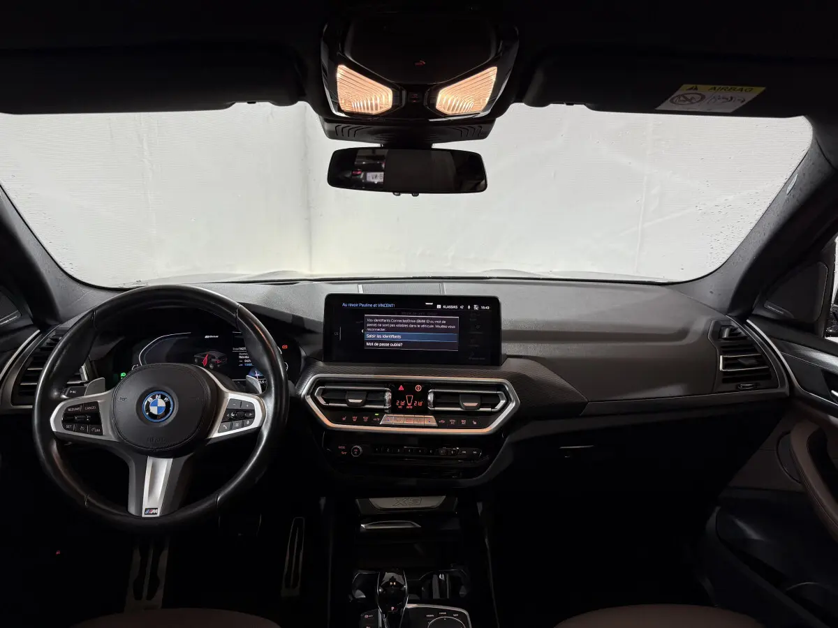 Intérieur BMW X3 xDrive30e 2023 vu de face, tableau de bord noir avec écran tactile central et volant cuir M Sport.