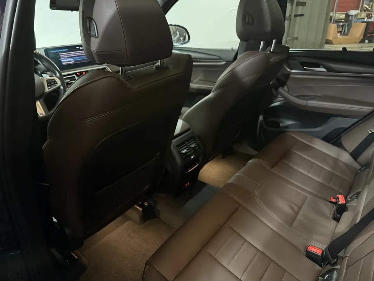 Intérieur arrière de BMW X3 bleu 2023, sièges cuir marron, console centrale avec aérateurs et commandes climatisation.