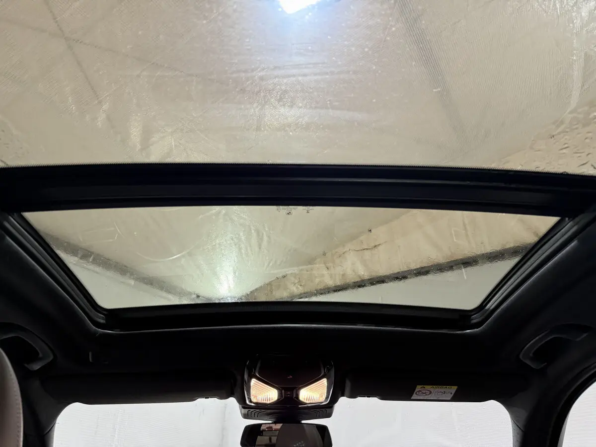 Toit ouvrant panoramique en verre vu de l'intérieur d'un BMW X3 bleu xDrive30e 2023, éclairage intérieur allumé.