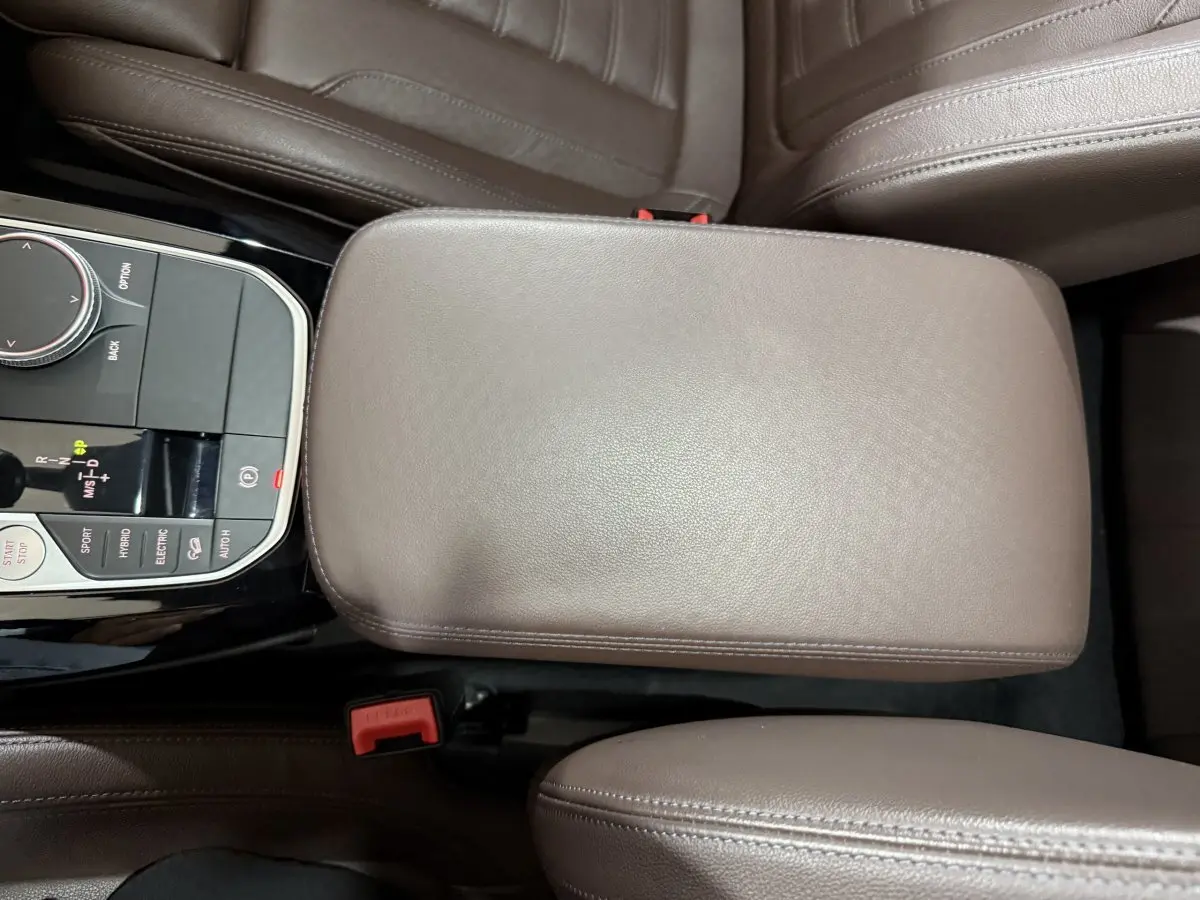 Vue plongeante sur l'accoudoir central en cuir marron et la console de commande du BMW X3 xDrive30e 2023.