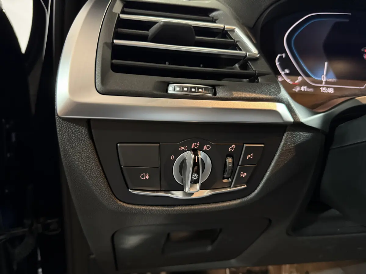 Gros plan sur le tableau de bord côté gauche du BMW X3 bleu 2023, montrant les commandes des phares et la ventilation.