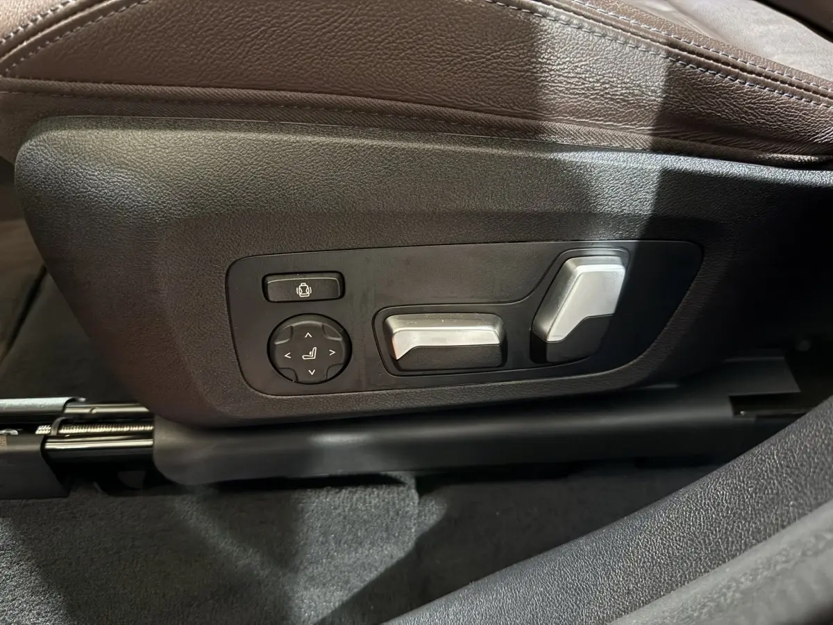 Gros plan sur les commandes électriques argentées du siège avant en cuir marron d'un BMW X3 bleu hybride rechargeable 2023.