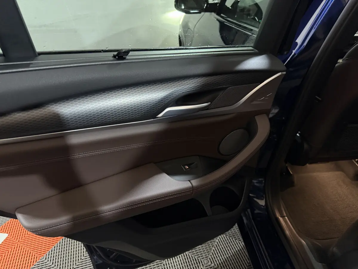 Intérieur de la porte arrière droite du BMW X3 xDrive30e bleu 2023, avec garniture cuir marron et détails noirs.