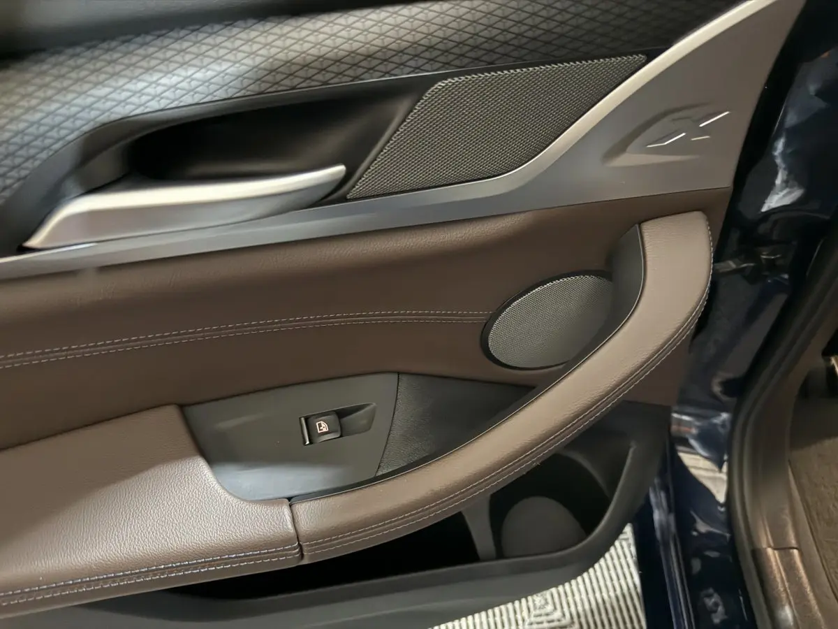 Détail de la portière avant gauche bleu foncé du BMW X3 xDrive30e avec garniture cuir marron et bouton de verrouillage.