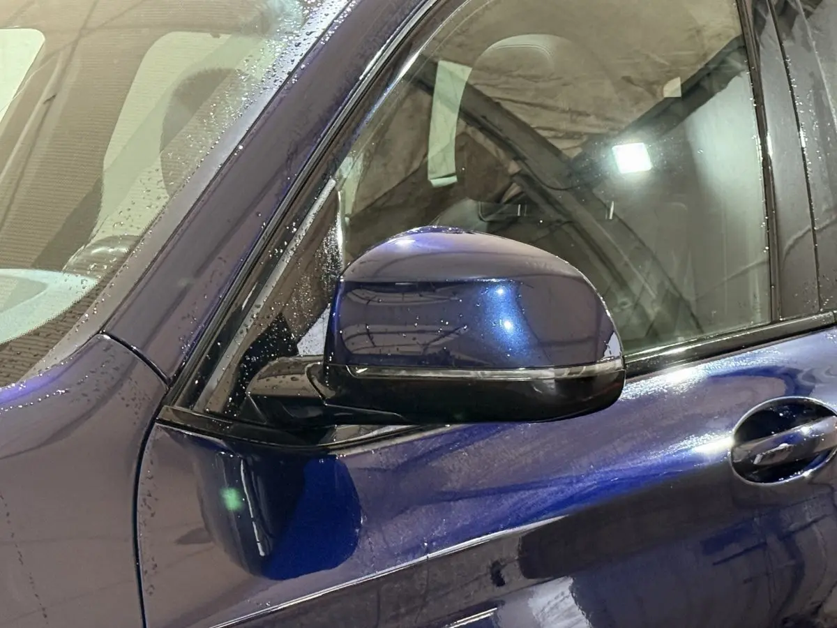 Gros plan sur le rétroviseur côté gauche d'un BMW X3 xDrive30e bleu 2023 avec gouttes d'eau visibles sur la carrosserie.