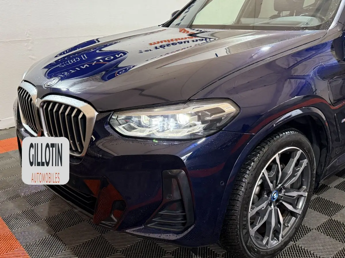 Vue 3/4 avant droit d'un BMW X3 bleu avec phares LED allumés et jantes alliage distinctives.