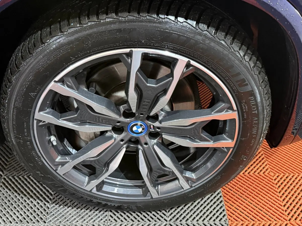 Gros plan sur la jante alliage sombre à motifs géométriques du BMW X3 bleu 2023 avec logo central BMW.