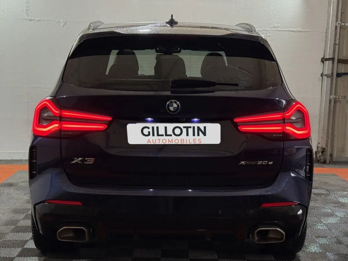 Vue arrière d'un BMW X3 xDrive30e bleu avec feux LED allumés et double sortie d'échappement carrée.