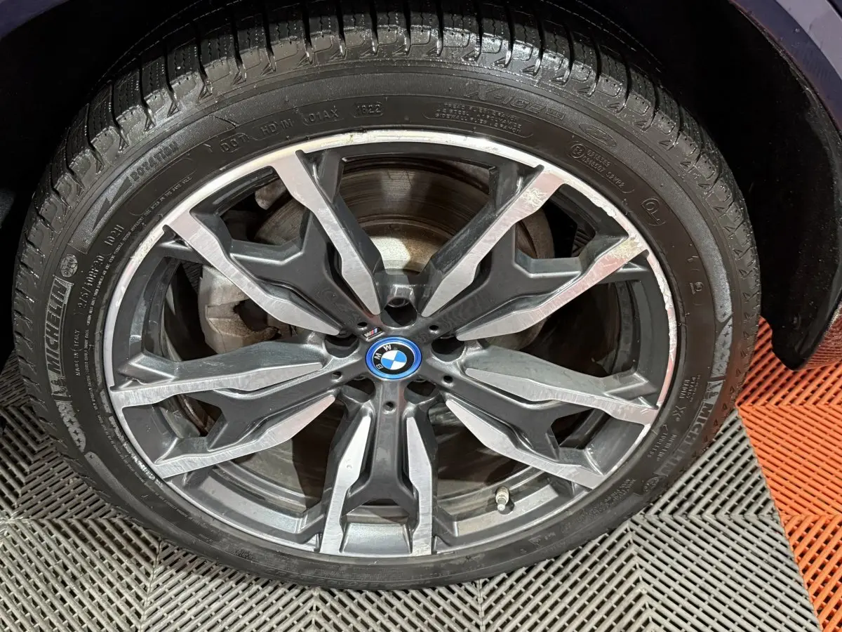 Gros plan sur la jante alliage grise au design complexe d’un BMW X3 bleu, mettant en valeur le logo central rond.