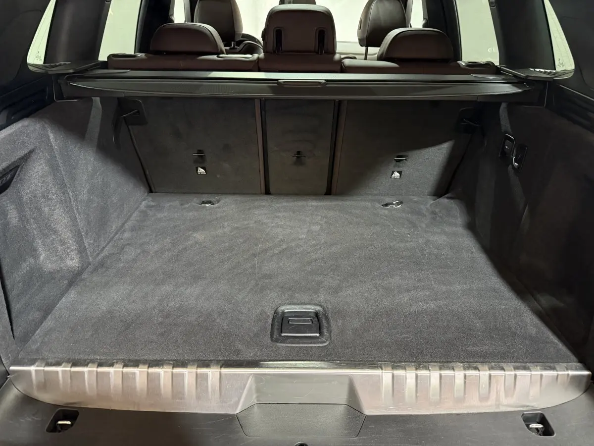 Coffre spacieux du BMW X3 xDrive30e bleu 2023 vu de l'arrière avec cache-bagages et sièges marron visibles.