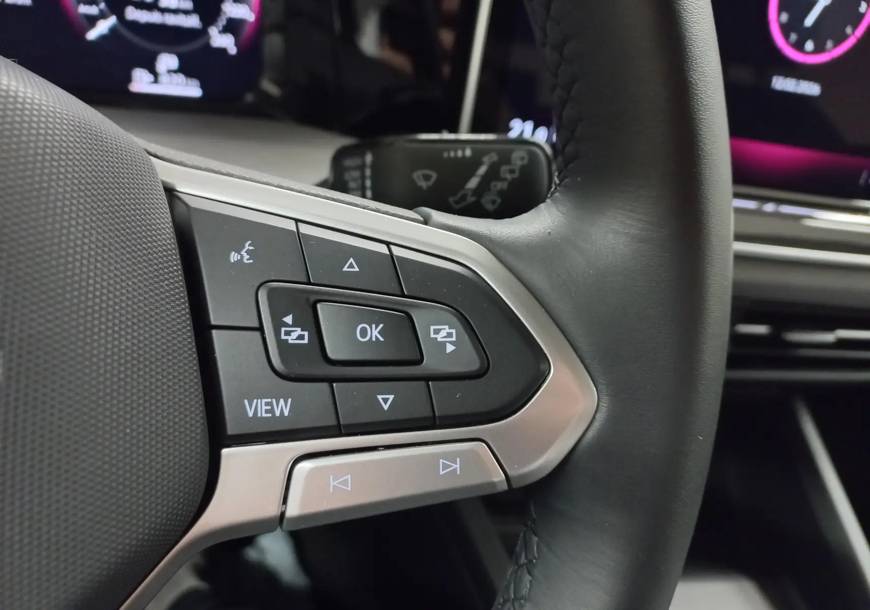 Gros plan sur les commandes au volant à gauche d’une Volkswagen Golf 1.5 eTSI 116 BVM6 Argent Dolomite, tableau de bord numérique visible.