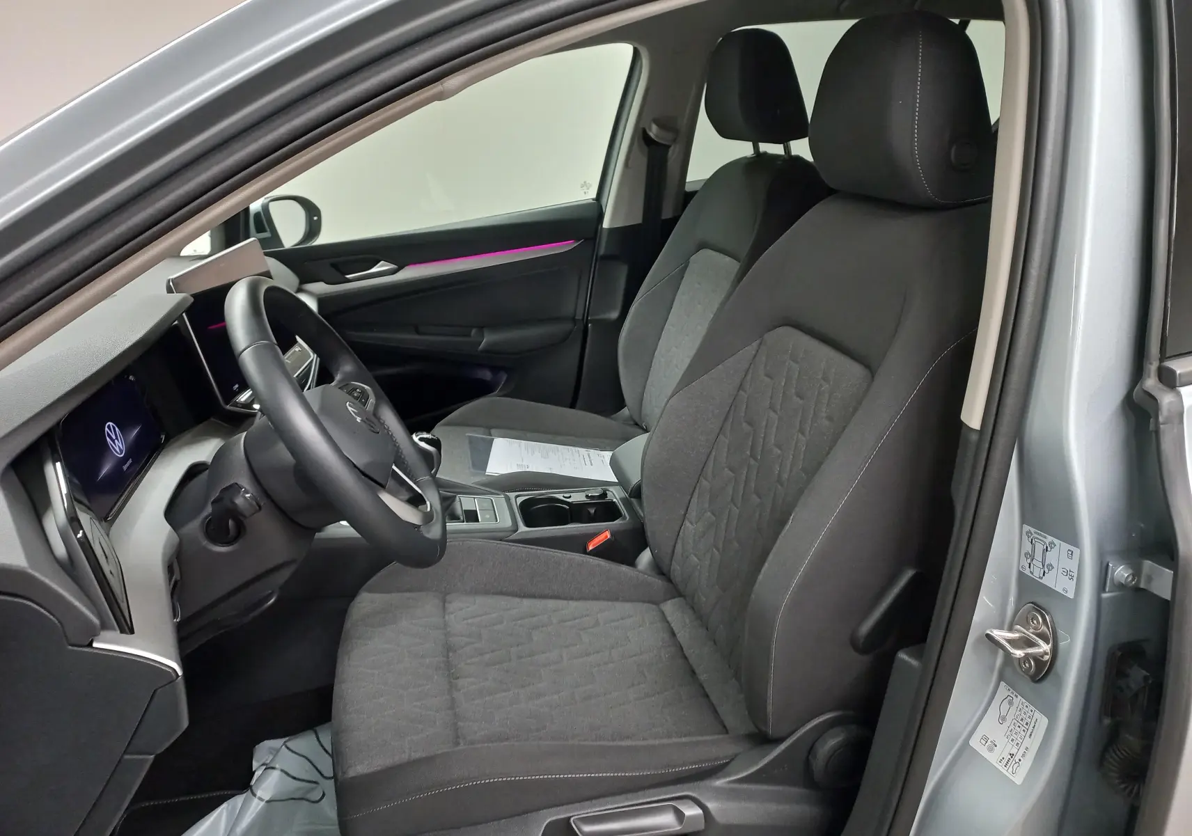 Vue intérieure côté conducteur de la Volkswagen Golf 1.5 eTSI 116 BVM6 argent Dolomite, sièges tissu gris et éclairage d'ambiance violet.