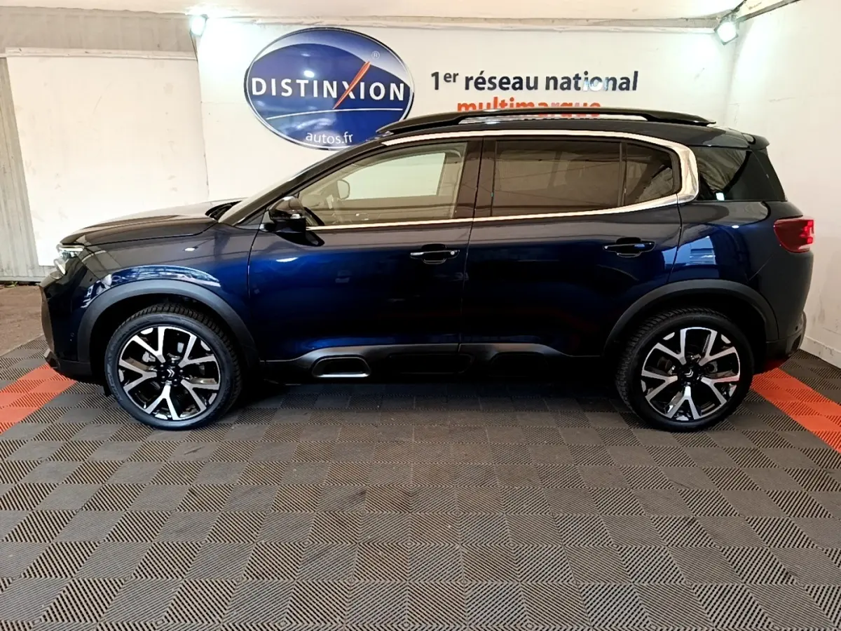 Vue de profil côté gauche d'un Citroën C5 Aircross 2023 bleu foncé avec jantes alliage et barres de toit noires.