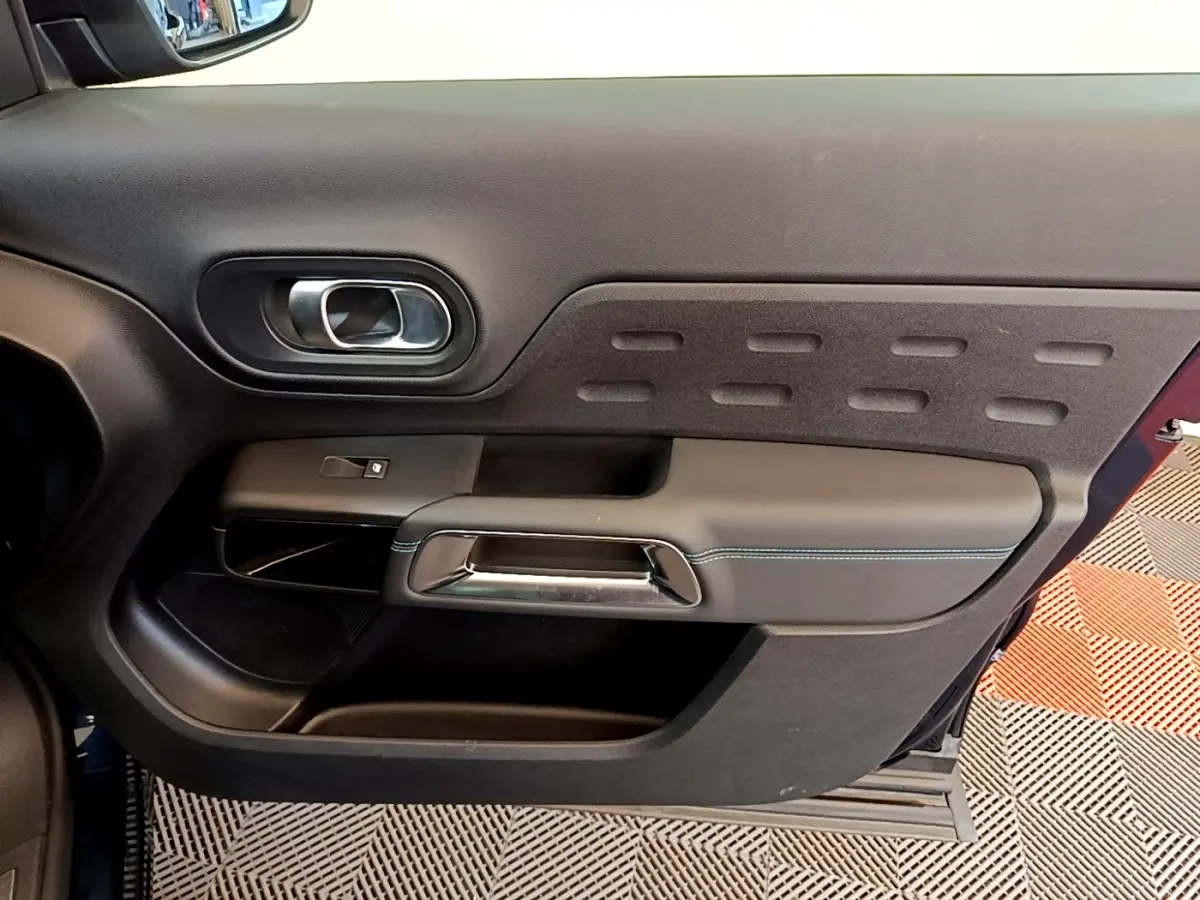 Vue intérieure côté gauche de la porte avant d’un Citroën C5 Aircross 2023 avec garniture noire et poignée chromée.