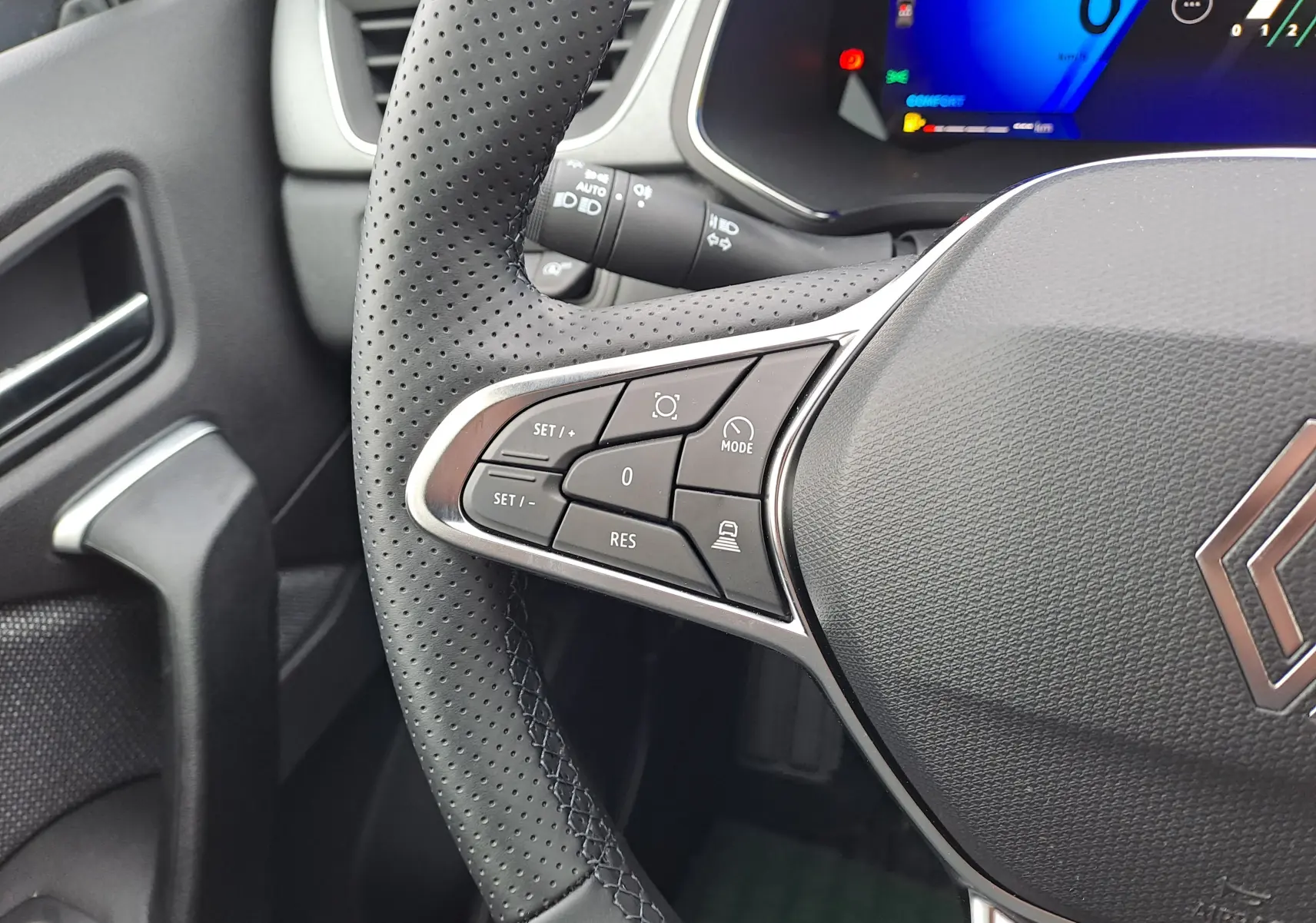 Gros plan sur le côté gauche du volant perforé noir du Renault Symbioz 2025 avec commandes intégrées et tableau de bord numérique bleu.