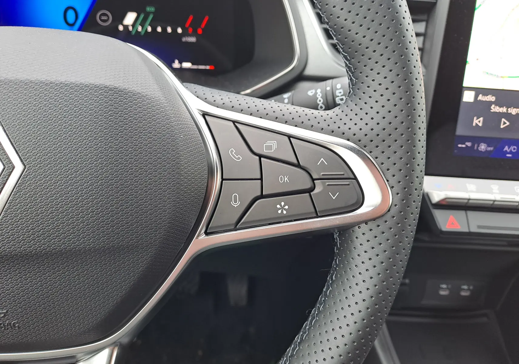 Gros plan sur le côté droit du volant perforé noir du Renault Symbioz bleu Mercure, avec commandes multifonctions visibles.