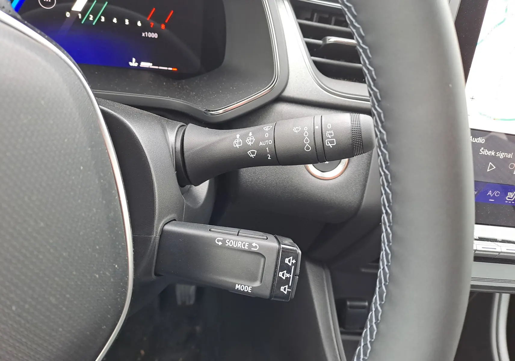 Gros plan sur la colonne de direction et les commandes derrière le volant d’un Renault Symbioz bleu Mercure, intérieur noir.