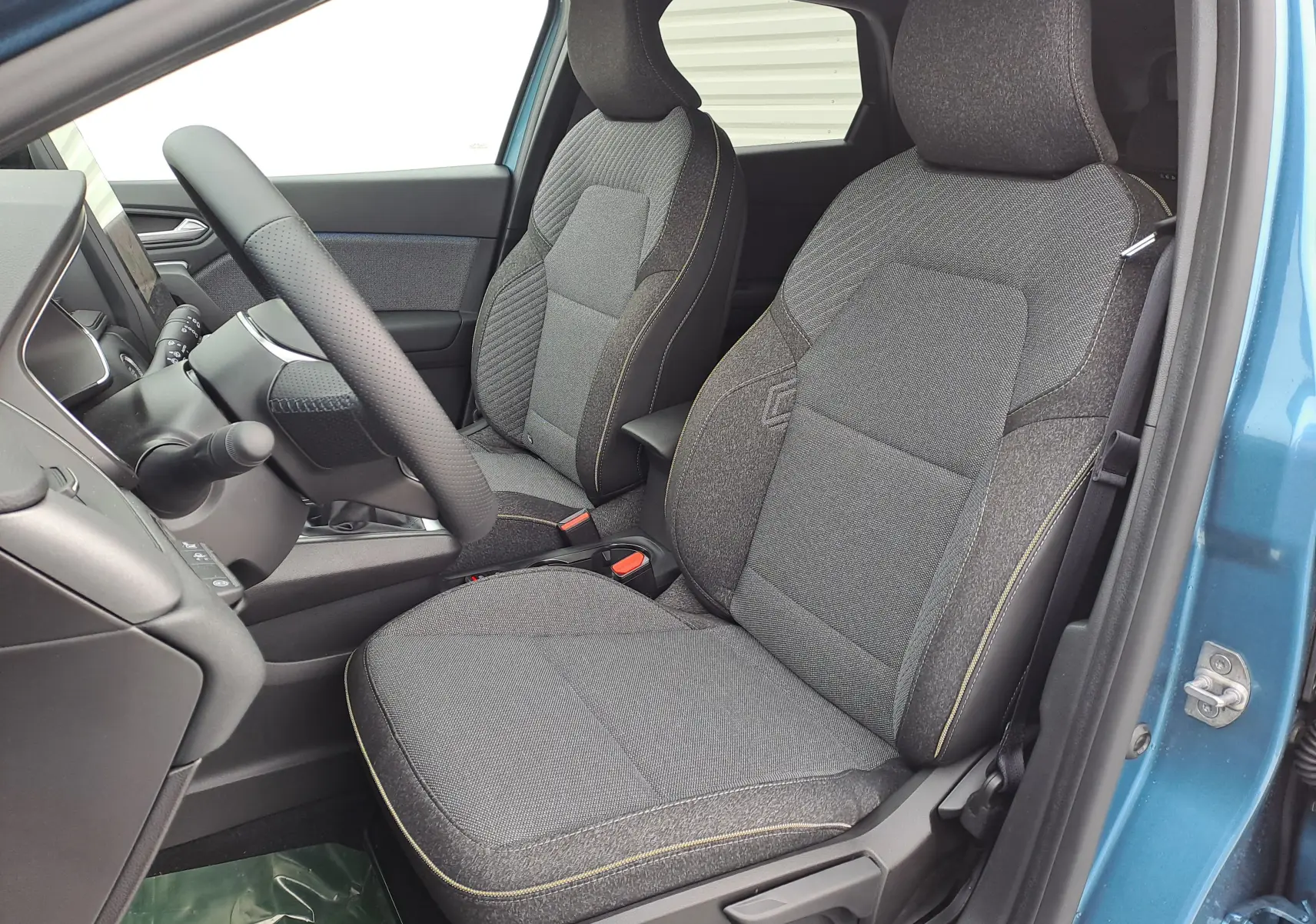 Vue intérieure côté conducteur du Renault Symbioz bleu mercure, mettant en valeur les sièges tissu gris avec surpiqûres jaunes.