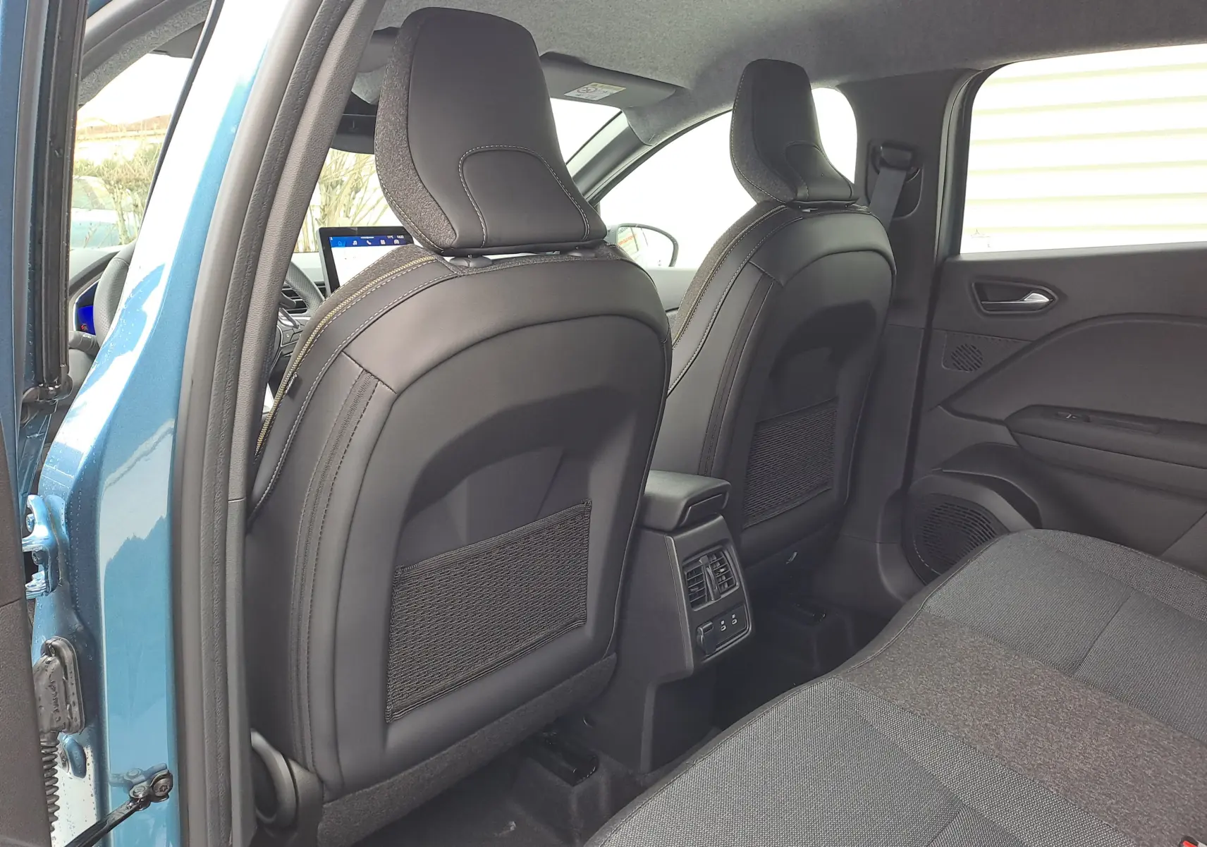 Vue intérieure arrière du Renault Symbioz bleu mercure 2025, montrant les dossiers noirs des sièges avant et la banquette tissu arrière.