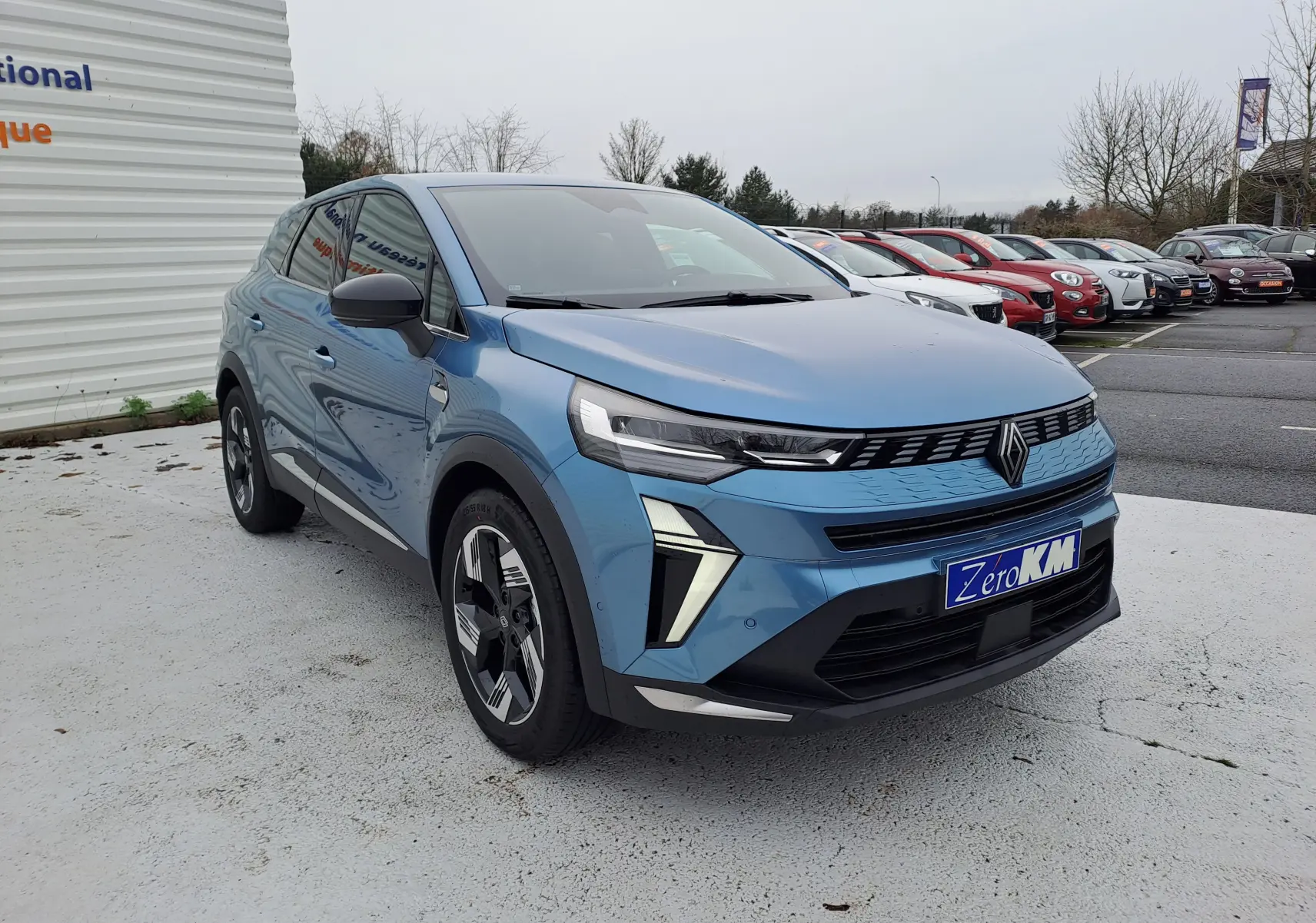 Renault Symbioz bleu mercure en 3/4 avant droit, avec calandre moderne et feux LED distinctifs sur parking.