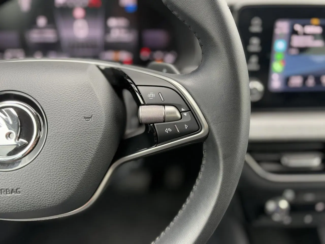 Gros plan sur le volant cuir multifonctions de la Skoda Scala 2024 avec commandes intégrées et tableau de bord flou en arrière-plan.
