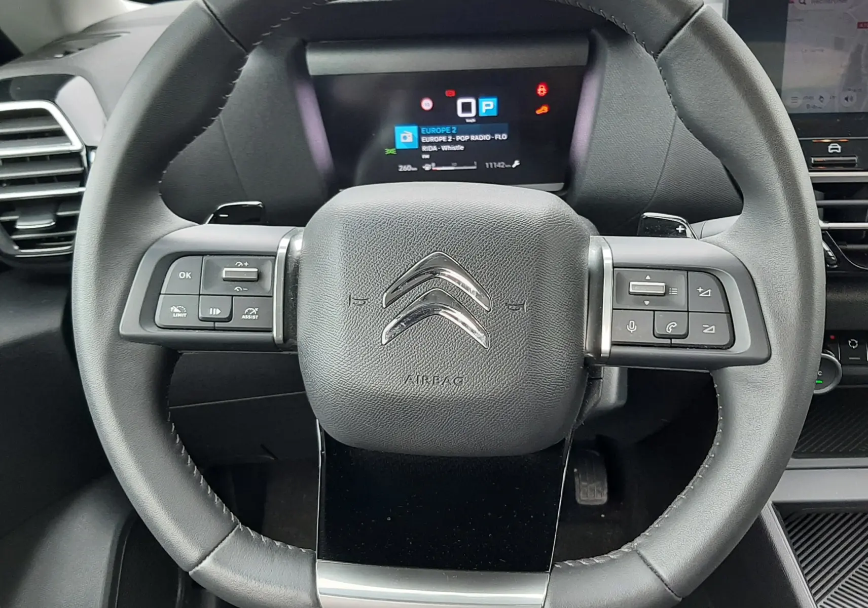 Vue rapprochée du volant noir de la Citroën C4 Hybrid 136 e-DSC6 Plus 2024 avec commandes intégrées et tableau de bord digital.