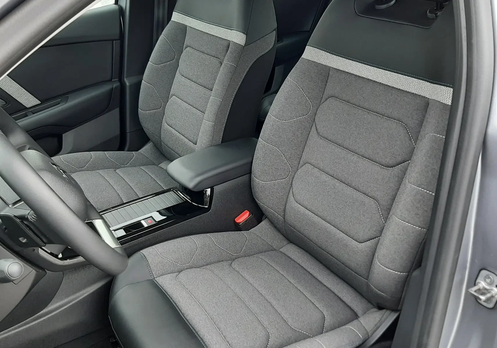 Vue intérieure côté conducteur de la Citroën C4 Hybrid 2024, sièges tissu gris avec surpiqûres et accoudoir central.