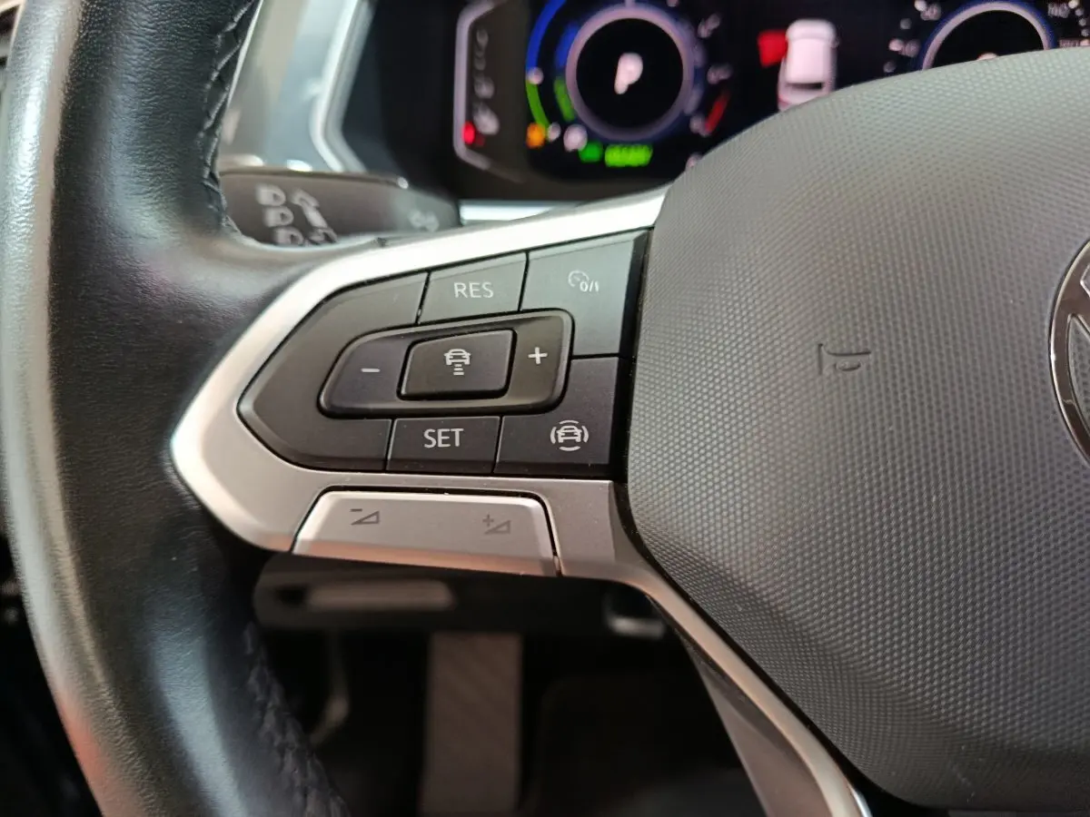 Gros plan sur les commandes du volant cuir à gauche du Volkswagen Tiguan bleu hybride rechargeable 2022.