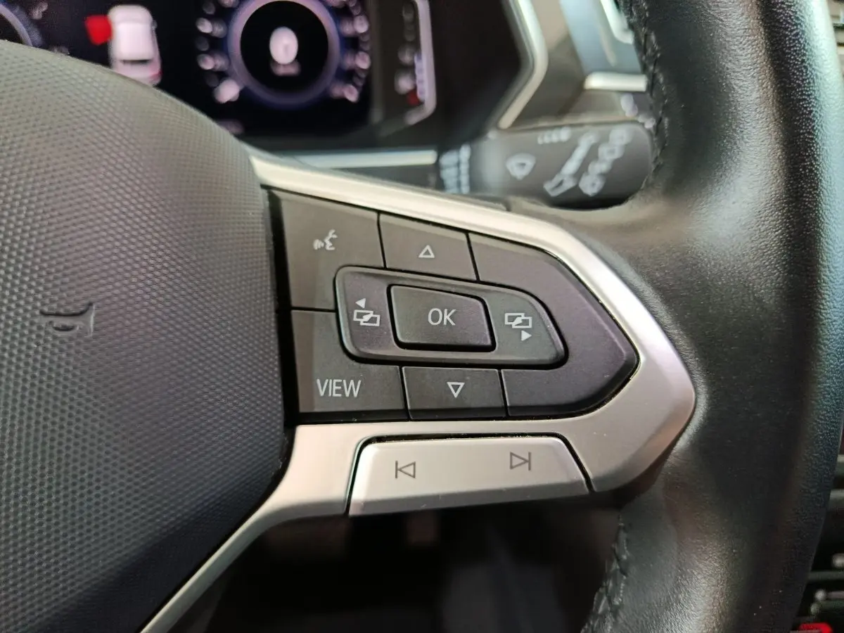Gros plan sur les commandes du volant cuir noir du Volkswagen Tiguan 2022, boutons multifonctions et affichage digital.