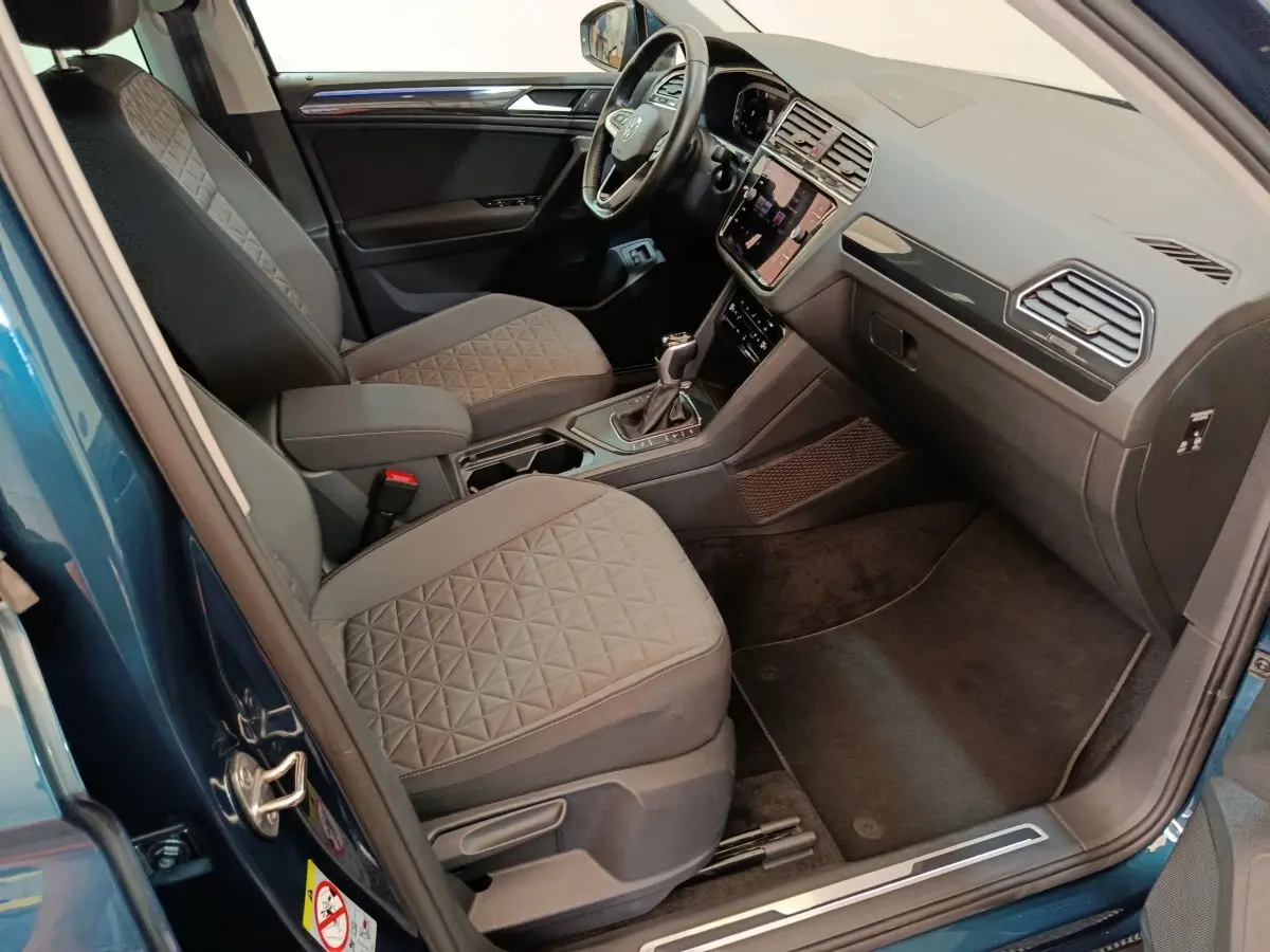 Intérieur côté conducteur du Volkswagen Tiguan bleu 2022, montrant sièges tissu gris et tableau de bord moderne.