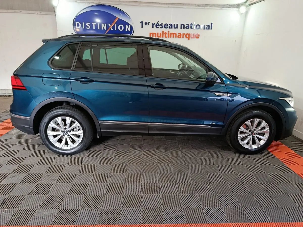 Profil côté gauche du Volkswagen Tiguan bleu 2022 hybride rechargeable, finition Life Business, en intérieur showroom.