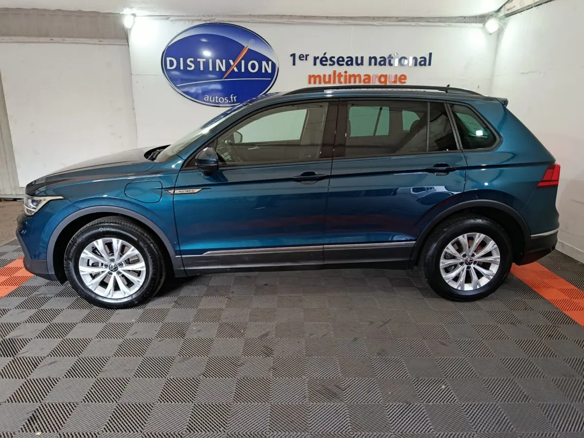 Profil côté gauche d'un Volkswagen Tiguan bleu hybride rechargeable 2022, avec jantes alliage et badge "Hybrid" sur aile avant.