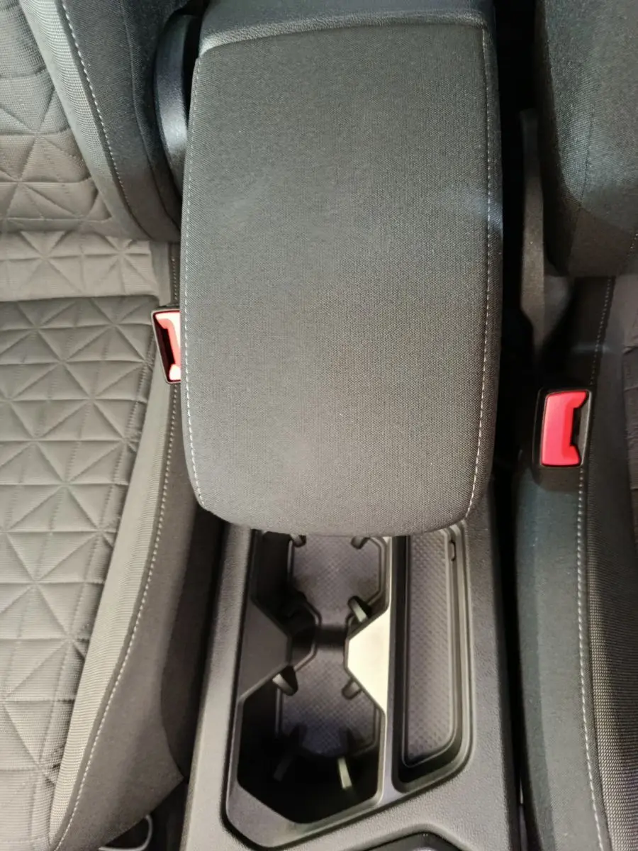 Vue plongeante sur l'accoudoir central et porte-gobelets noirs entre les sièges tissu gris du Volkswagen Tiguan hybride.