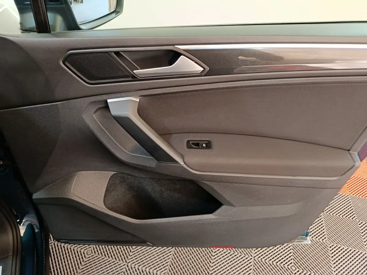 Gros plan sur la porte côté gauche du Volkswagen Tiguan bleu 2022, mettant en valeur la poignée et les finitions intérieures noires.