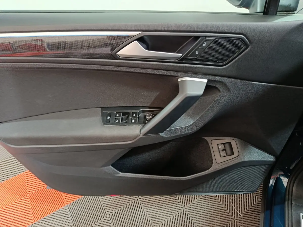 Vue rapprochée de la porte avant gauche du Volkswagen Tiguan bleu 2022, avec commandes électriques et finition noire.