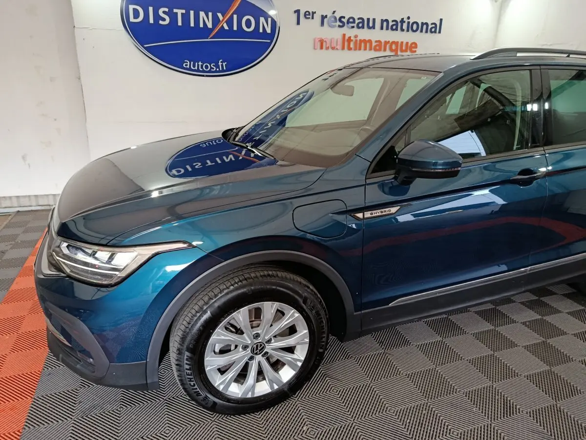 Vue 3/4 avant droit d'un Volkswagen Tiguan bleu hybride rechargeable avec badge "eHybrid" sur aile avant.