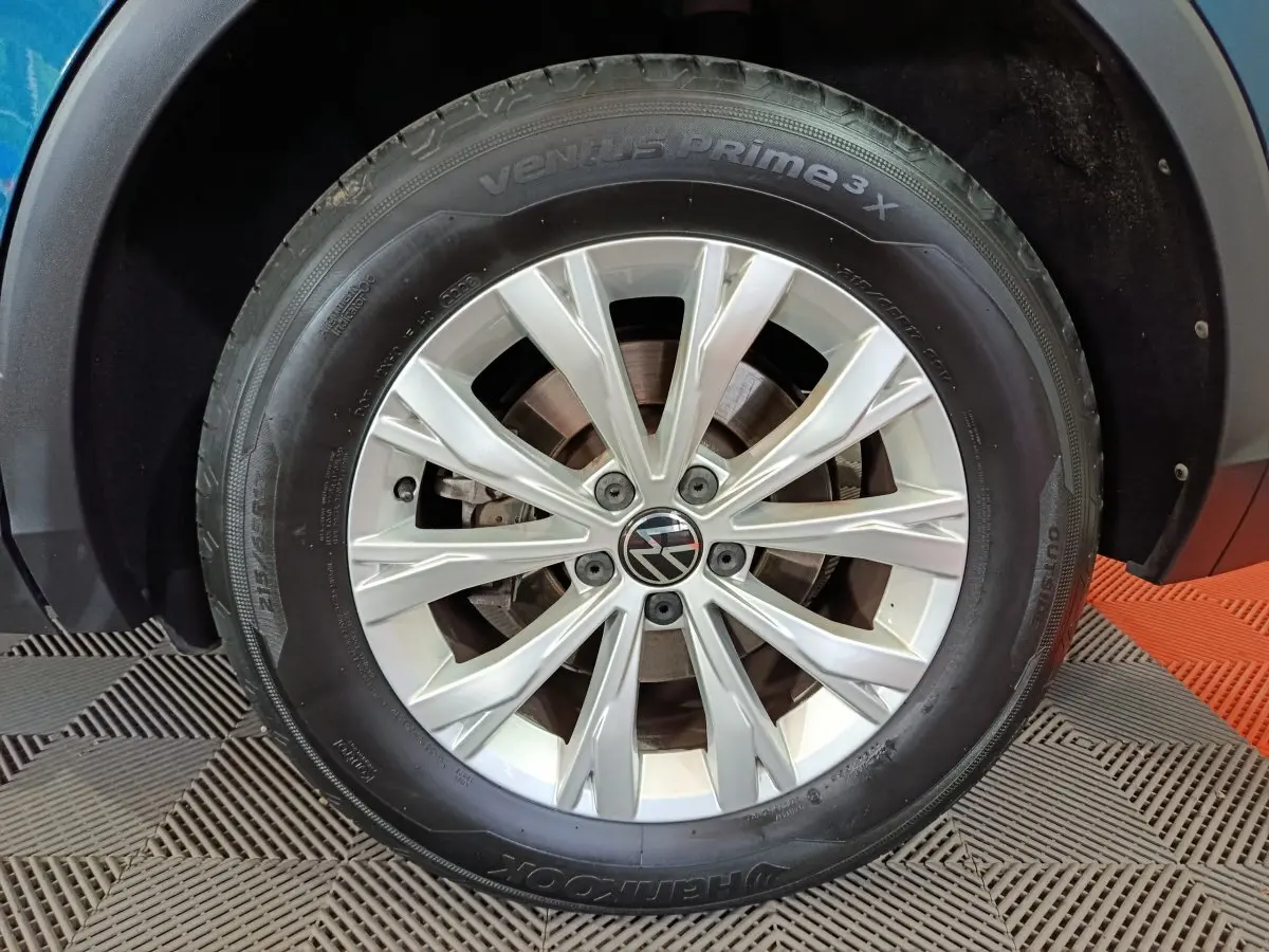 Gros plan sur la roue avant gauche du Volkswagen Tiguan bleu, mettant en valeur la jante argentée et le logo VW central.