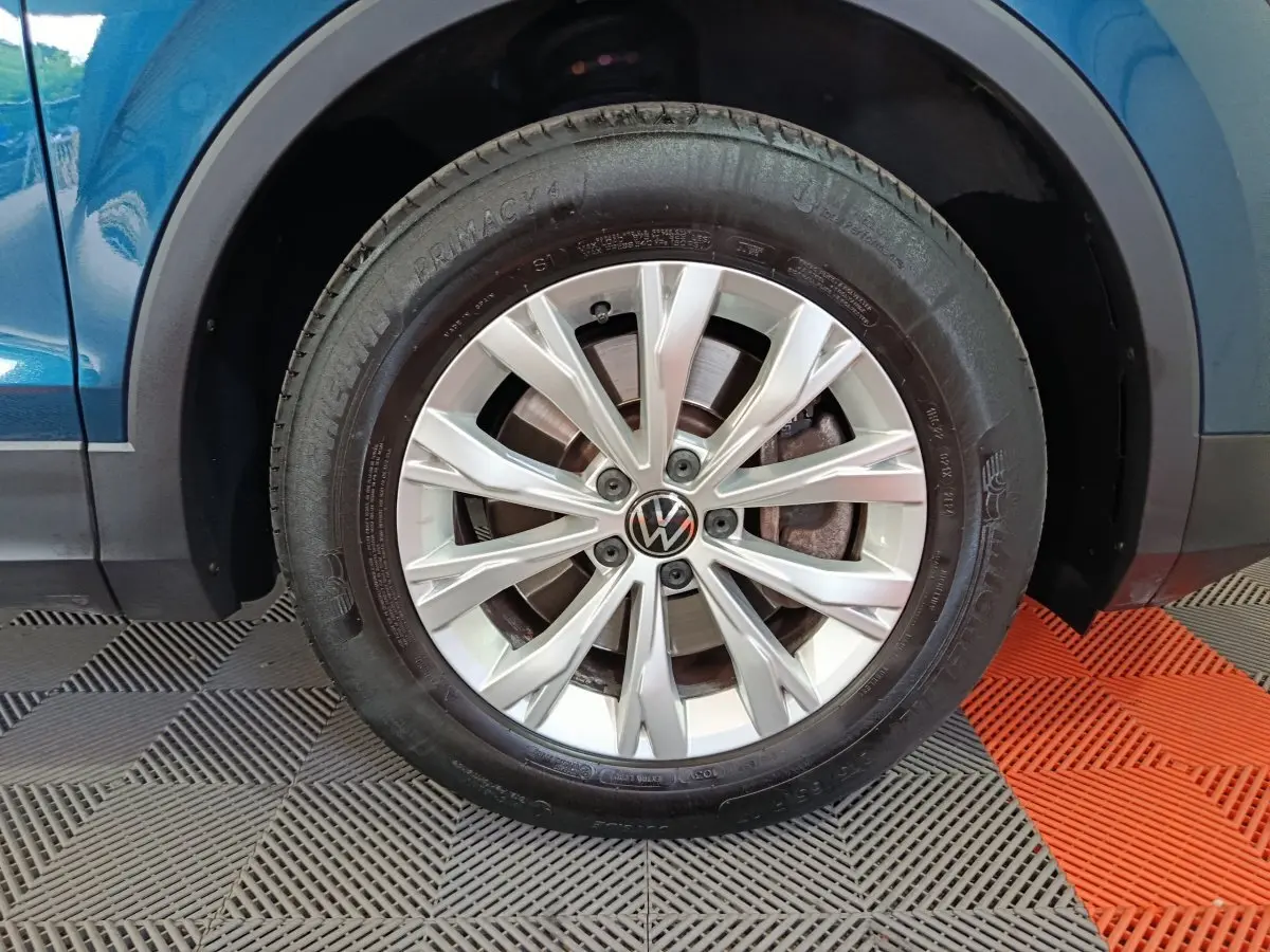 Gros plan sur la roue avant gauche d’un Volkswagen Tiguan bleu 2022 avec jante alliage argentée et logo VW central