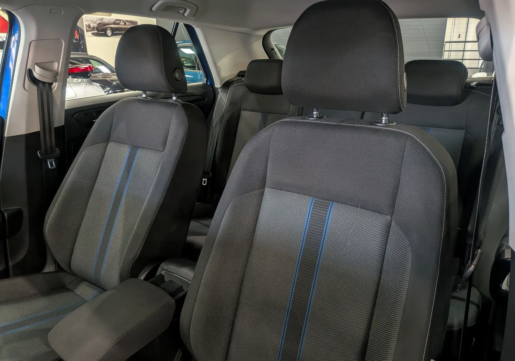 Vue intérieure des sièges avant et arrière du Volkswagen T-Roc 2018, tissu gris avec bandes bleues, habitacle lumineux.